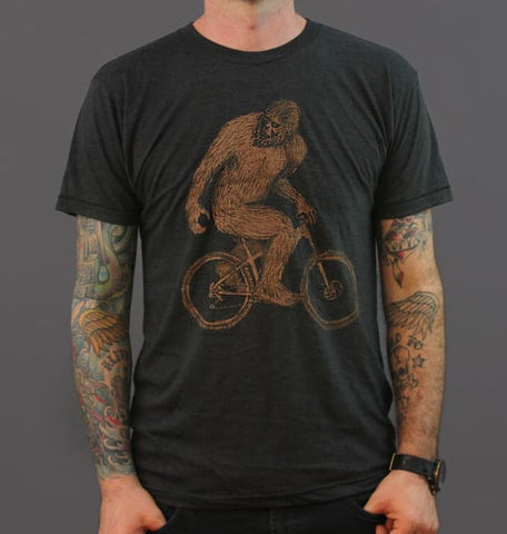 black shirt with a screen printed sasquatch riding a bicycle